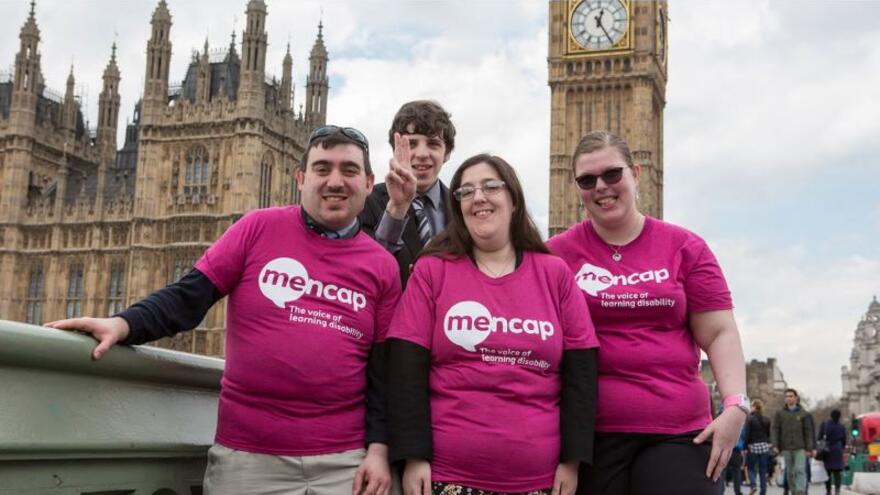 Group of four people stood together wearing Mencap t-shirts, in front of the Houses of Parliament