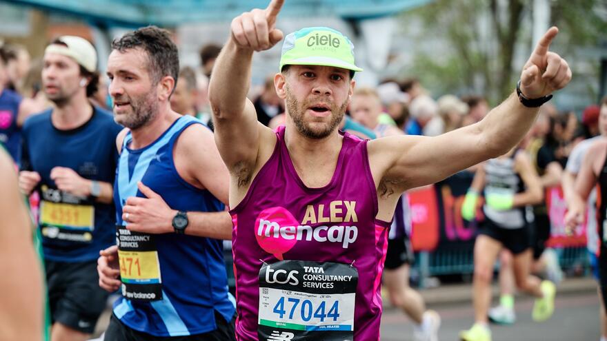 Mencap runner with pink running vest and hands up in the air