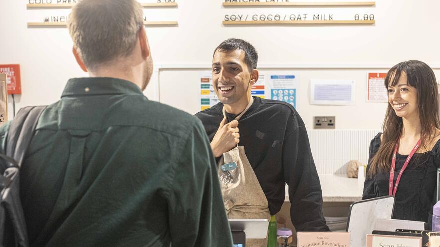 Supported internship learner, Zaki serves a customer at Fair Shot Cafe.