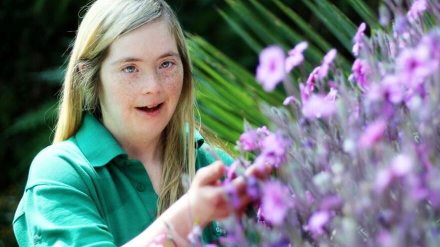 Girl with down syndrome smelling purple floweres in a garden