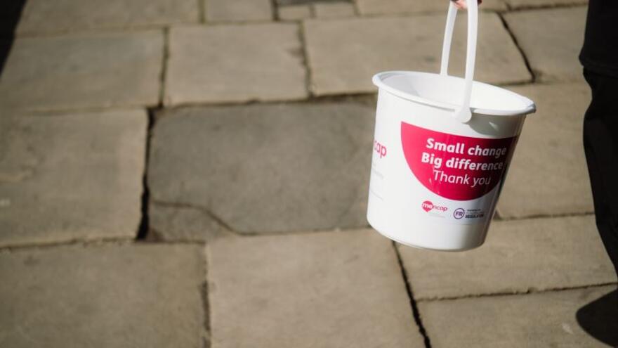 A picture of a Mencap collection bucket being carried down a street