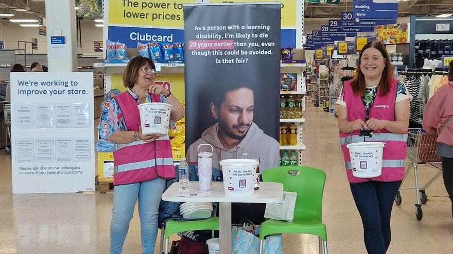 Two volunteers wearing Mencap hi-vis vest standing with buckets in Tesco
