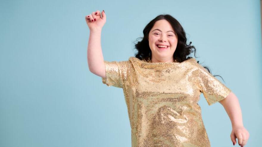 A head and shoulders photograph of Ellie modelling a gold dress