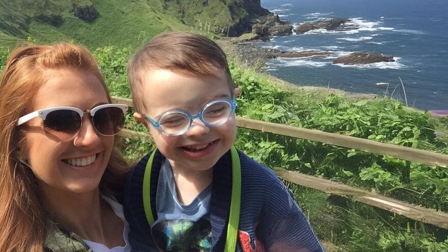 Odhran with his mother in front of a fence overlooking a cliff and beach below them