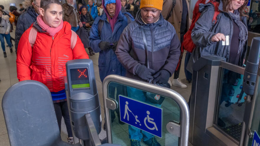 A person walking through a gate in a station with lots of people behind them.
