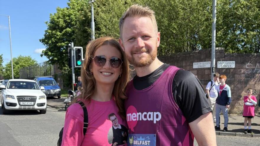 A man in a Mencap running vest hugs a woman in a street