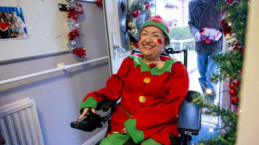 Lady in a Christmas elf costume smiling in a wheelchair at a ps service