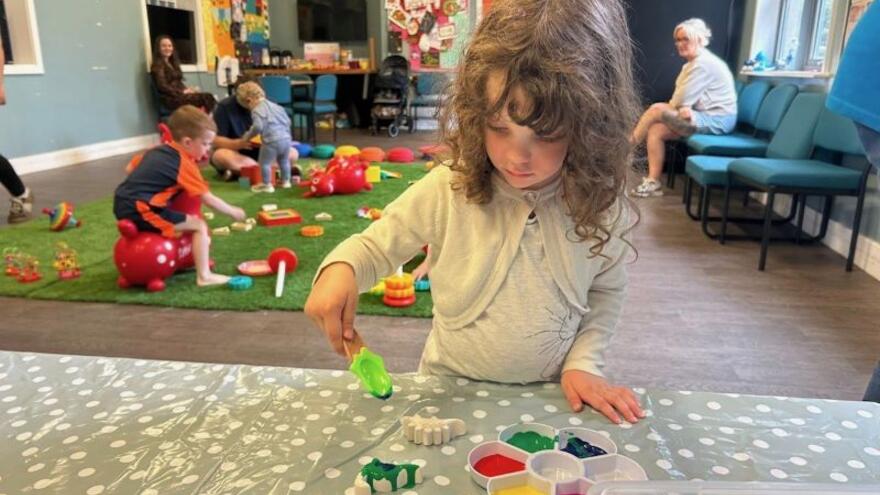 A girl painting at a table with other children sitting behind her