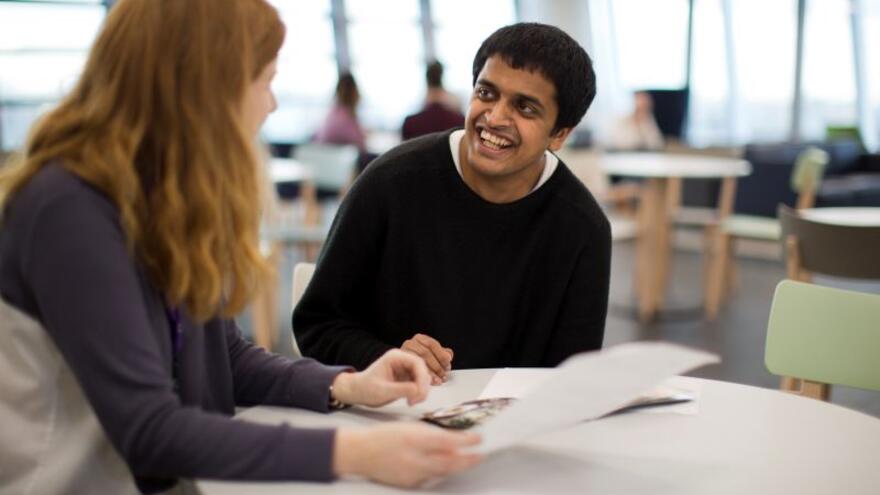 A young man and woman are sat talking at a desk in an office