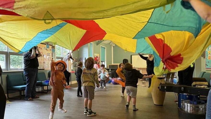 Children and support workers playing in a community room with a parachute