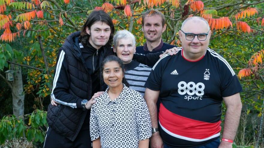 Five people grouped together, standing outside with an autumn tree in the background
