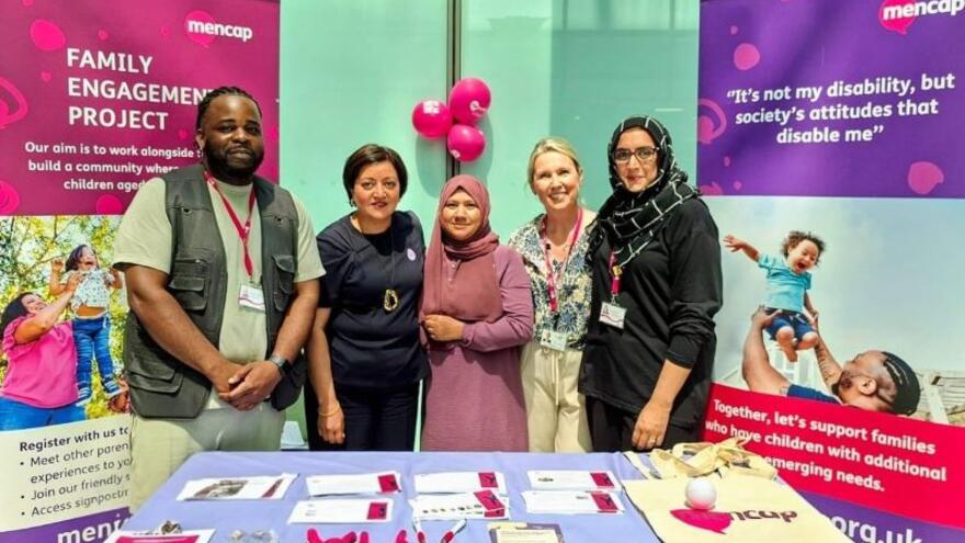 a group of people next to some Mencap posters and a table with Mencap merchandise