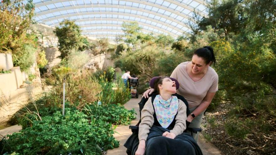 Emma who has cerebal palsy being pushed in her wheelchair by her carer in a botanical garden