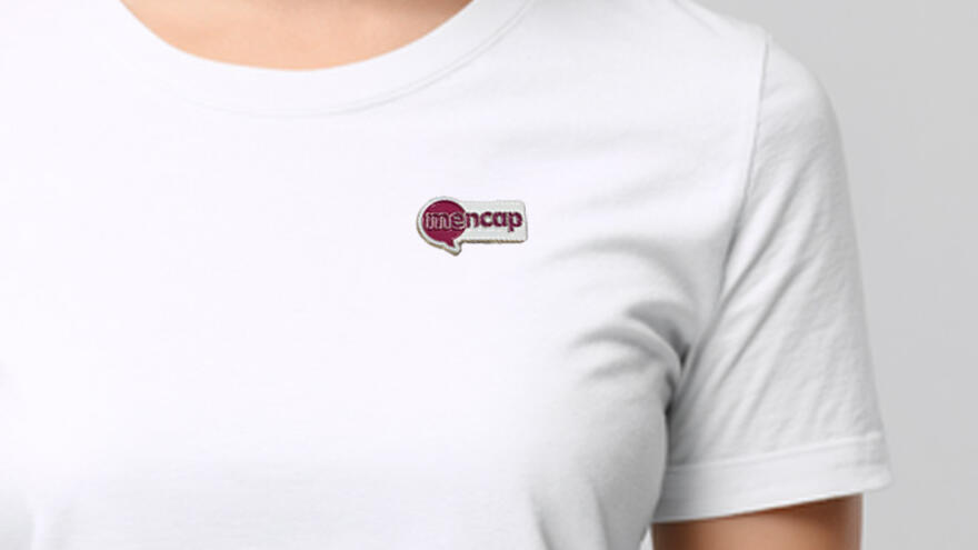 A Mencap pin badge being worn by someone in a plain white Tshirt
