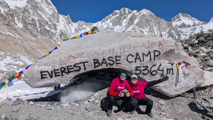 Man and woman squat down next to a rock that says Everest Base Camp