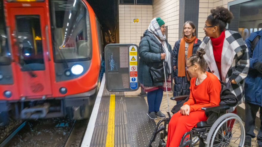 A photograph of a tube train coming into a station and a woman in a wheelchair on the platform