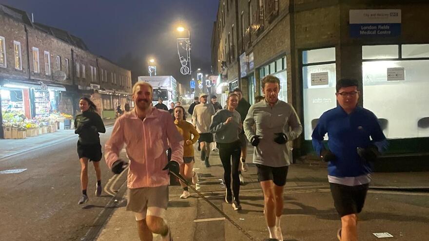 Mixed gender group of runners running in the dark through a city.