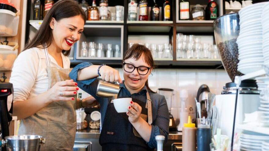 A woman watching a woman fill a coffee cup behind a counter in a coffee shop