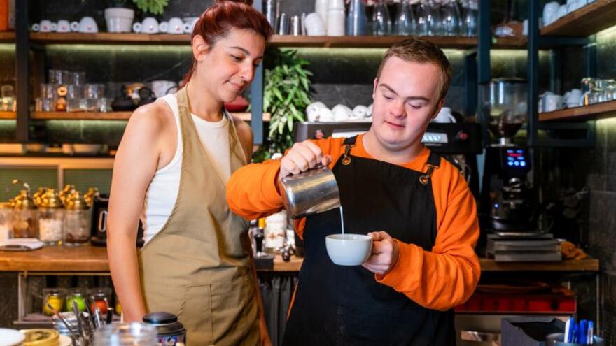 A woman watching a man fill a coffee cup behind a counter in a coffee shop