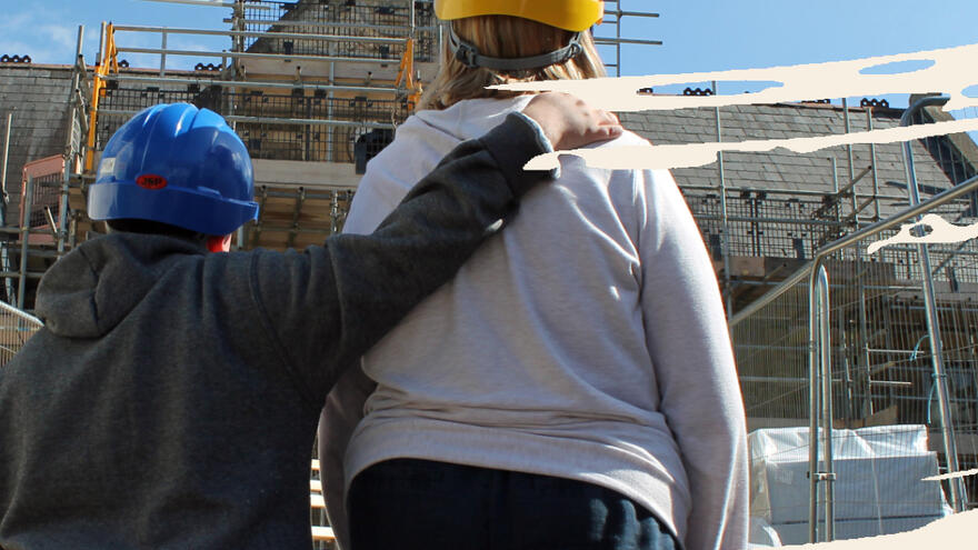 Two people wearing hard hats staring at a Victorian school which is being renovated