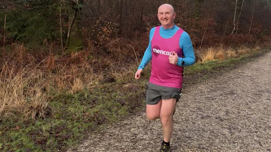 Man running in the woods in a pink Mencap vest