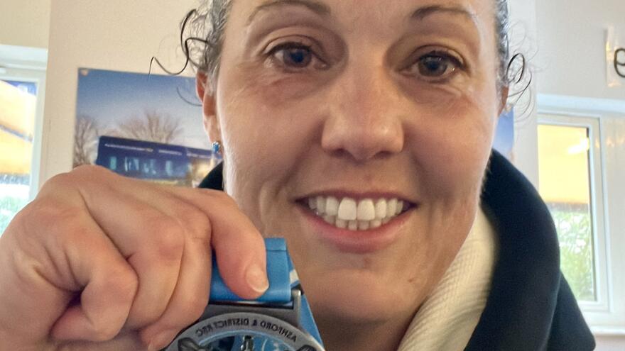 Woman smiling holding up a running medal