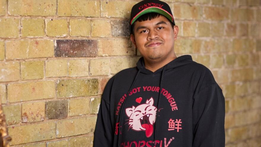 Arjhay in a chopstix sweatshirt and cap leaning against a brick wall