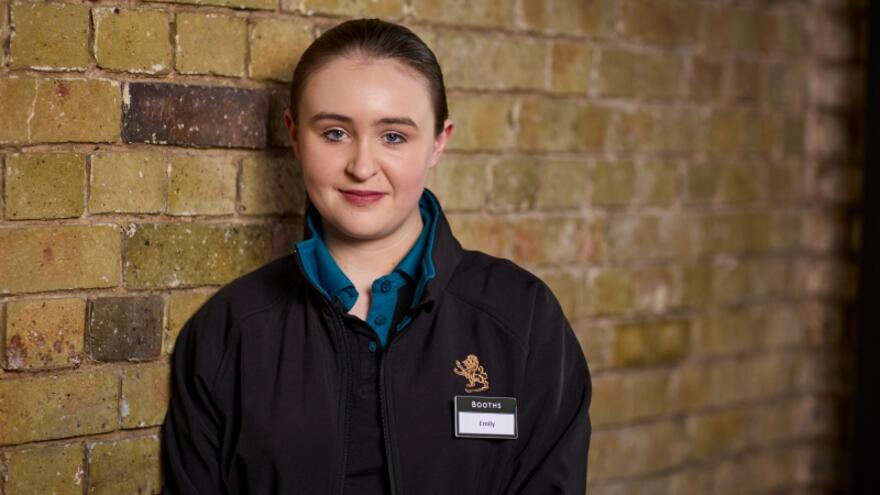 Emily in her Booths supermarket uniform standing in front of a brick wall