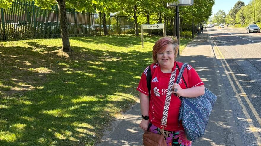 Myth Buster Heidi wearing a red t-shirt walking on a sunny day along a path with grass and trees behind her