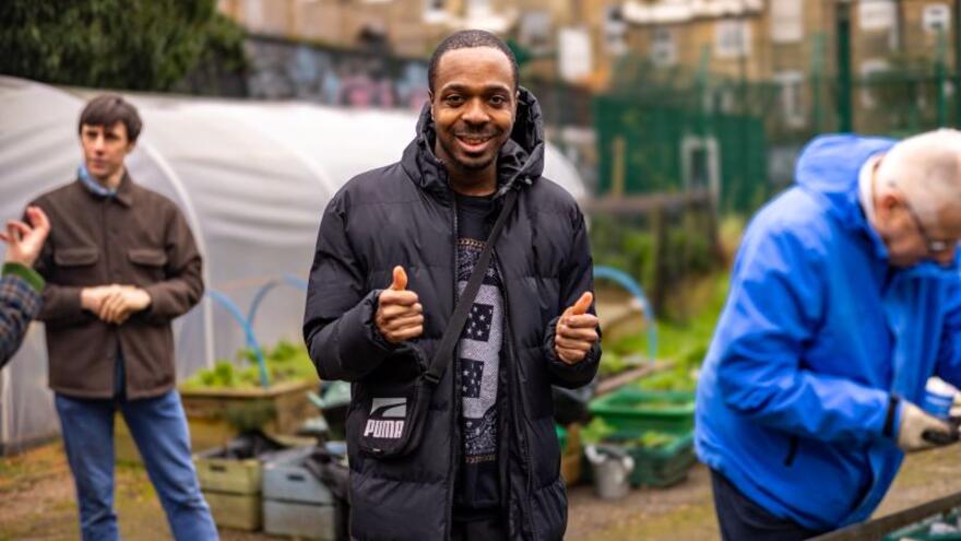 A man doing a thumbs up in a garden where people are gardening