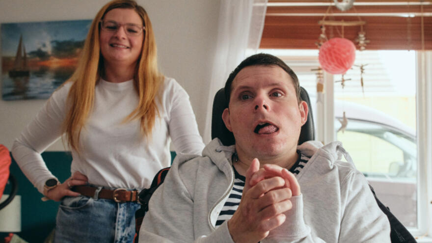 A man in a wheelchair at a Mencap service with a Mencap support worker standing behind him