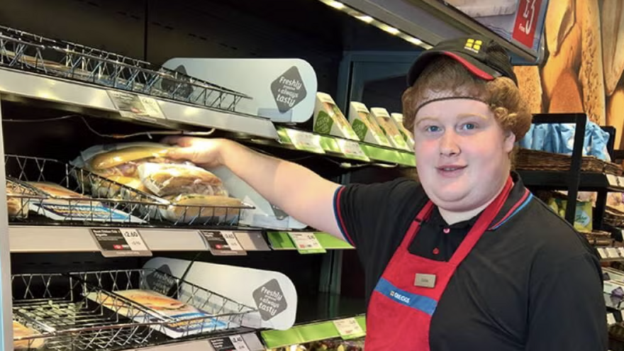 Eddie in a Greggs uniform restocking the shelves