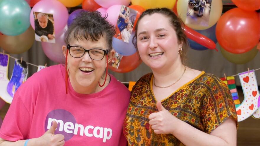 Two women volunteers at Mencap smiling with their thumbs up