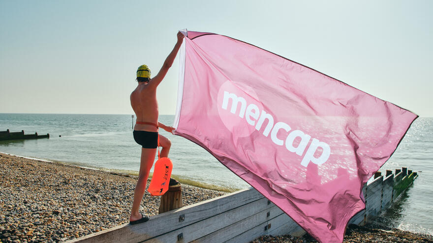 Person in swimming costume holding giant Mencap flag