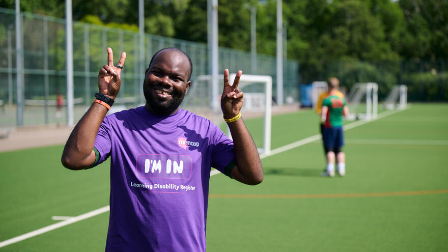Mencap and MPs football match - a Mencap player in a purple shirt smiles and makes the peace sign