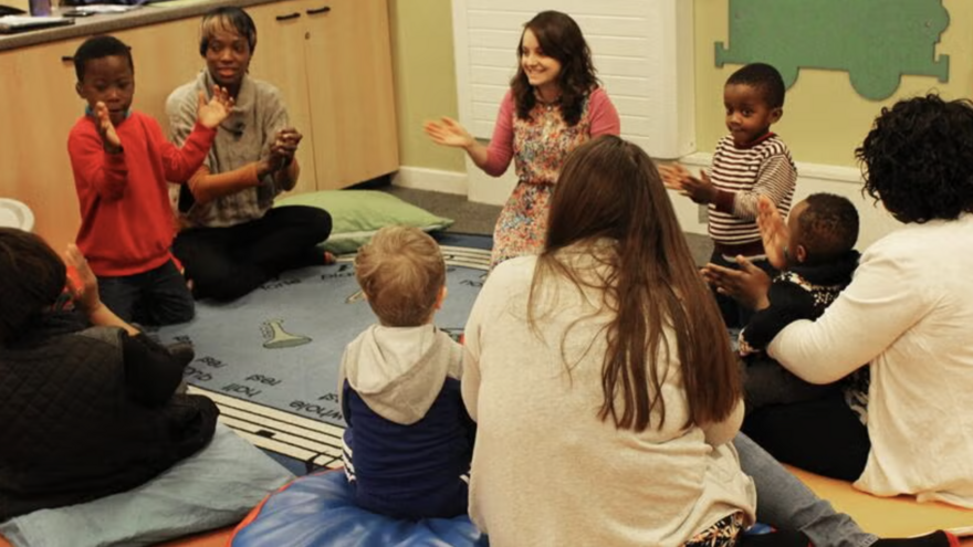 A school group of young children with their parents sitting in a circle clapping their hands