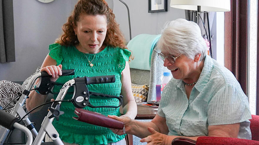 A support worker kneeling down helping a woman in a chair with her purse