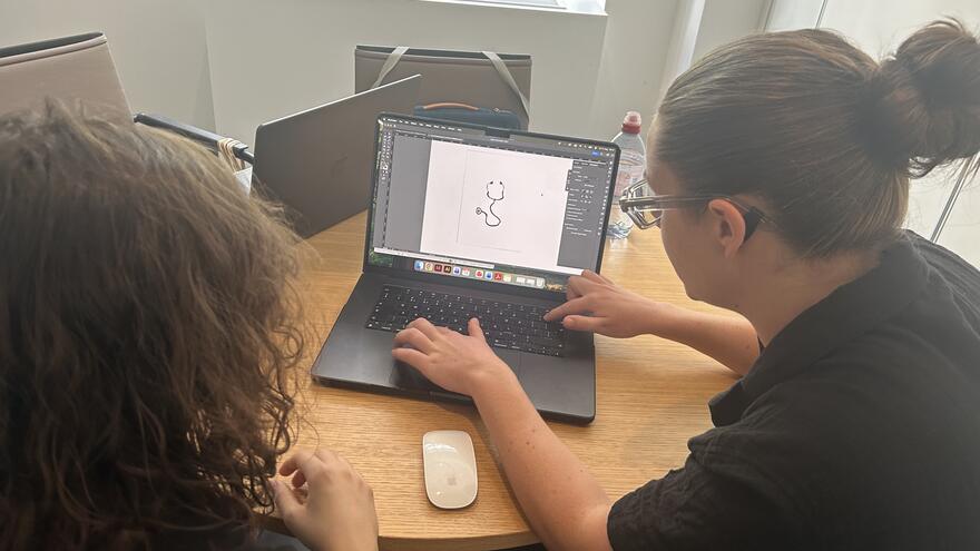 Josh and Annie are both looking at a sketch on a laptop screen in the Mencap office