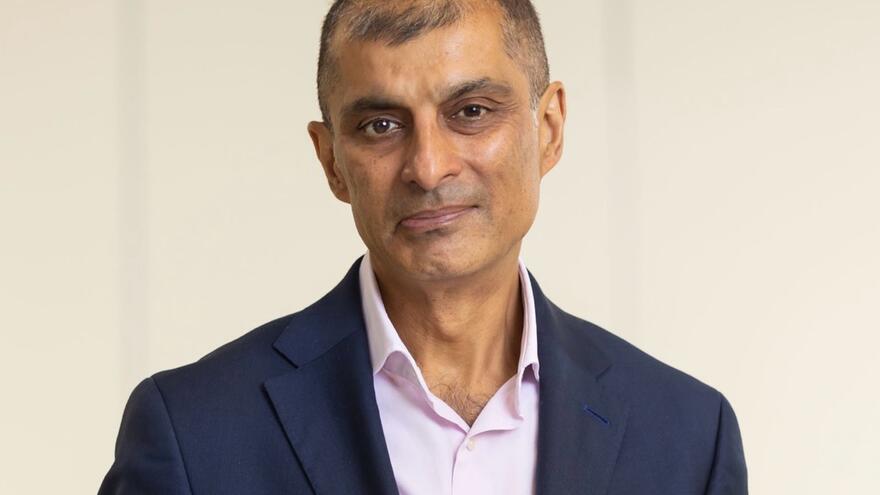 Mencap Trustee, Jitesh Sodha wears a navy suit in an office room