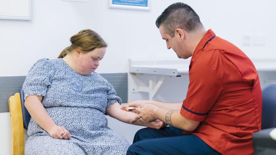 A male nurse doing a blood test on a young woman with Down Syndrome