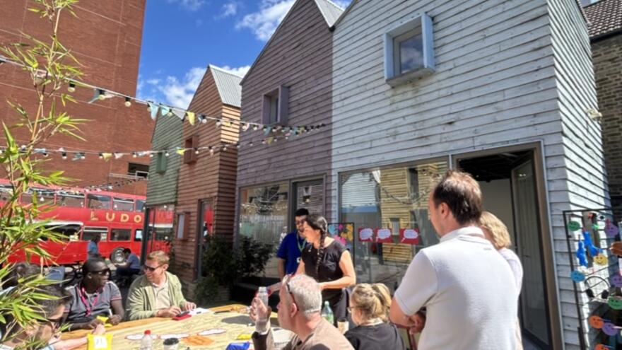 The outside of the exhibition space in London with people sat at picnic benches