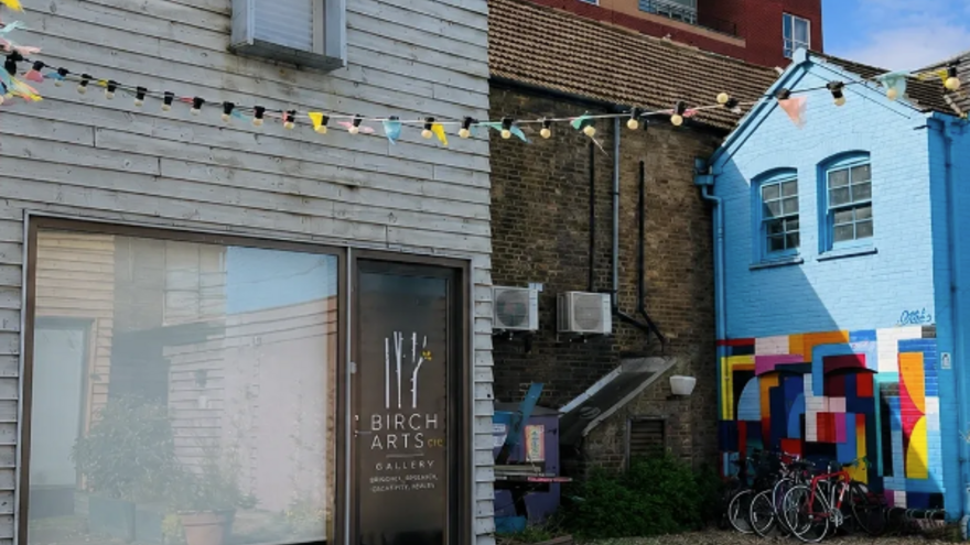 A building with wooden cladding on the outside and a sign for: Birch Arts on the door
