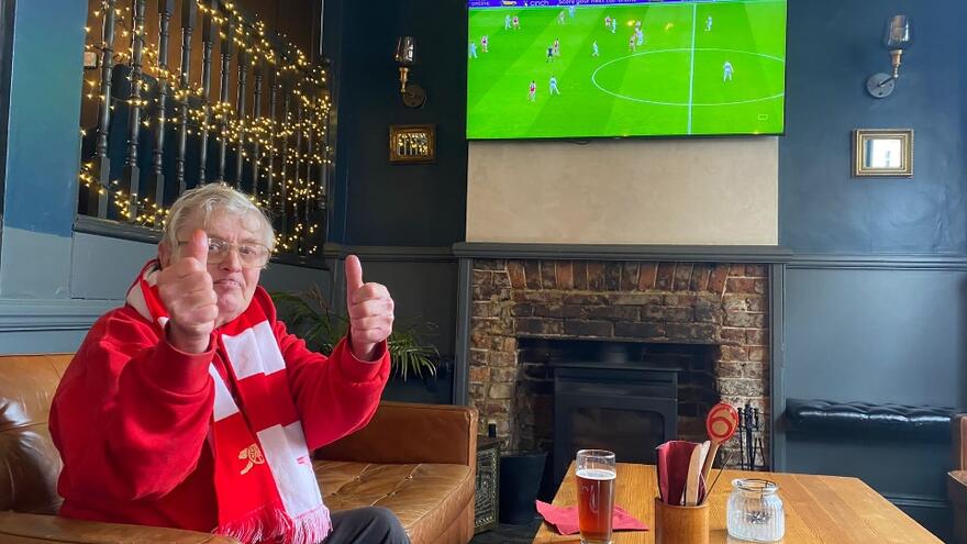 A man in a red and white scarf watching a football match on TV