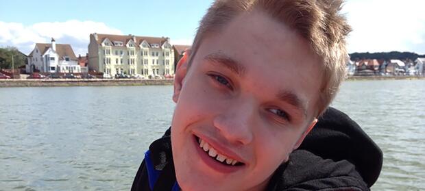 Young man stood outside on waterfront, smiling.