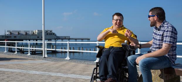 Two men sat smiling in front of seafront.