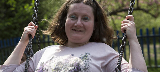 Woman with shoulder-length brown hair swinging on swing in park.
