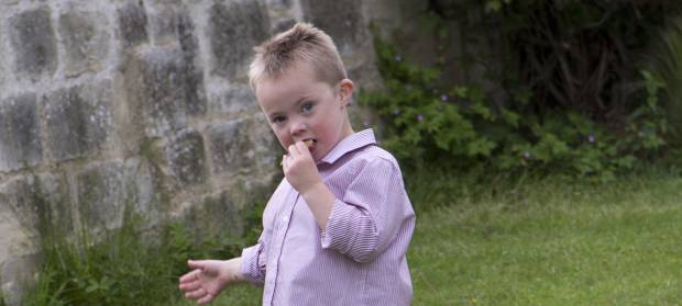Young boy stood in garden holding biscuit in his mouth.
