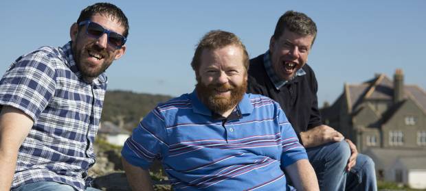 Three men laughing together whilst sat outside on a sunny day.