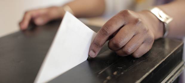 Hand placing voting slip in a ballot box.