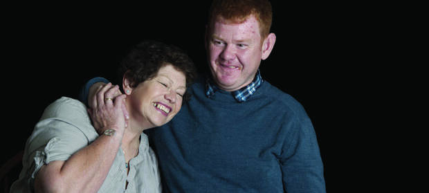 Man and woman stood together smiling. The man has his arm around the woman's shoulder.